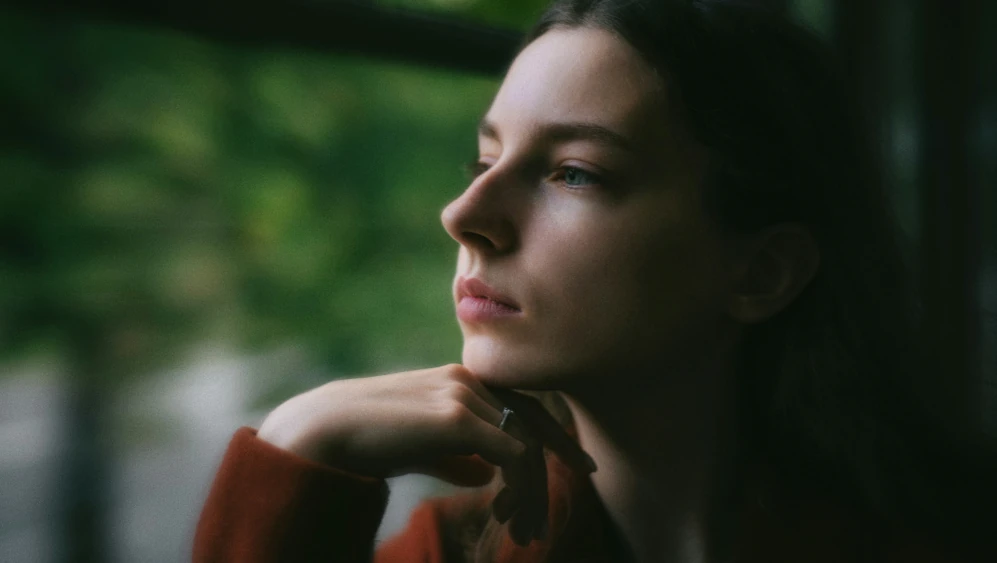 Woman looking thoughtfully out of a window, reflecting on childhood trauma and emotional impact.